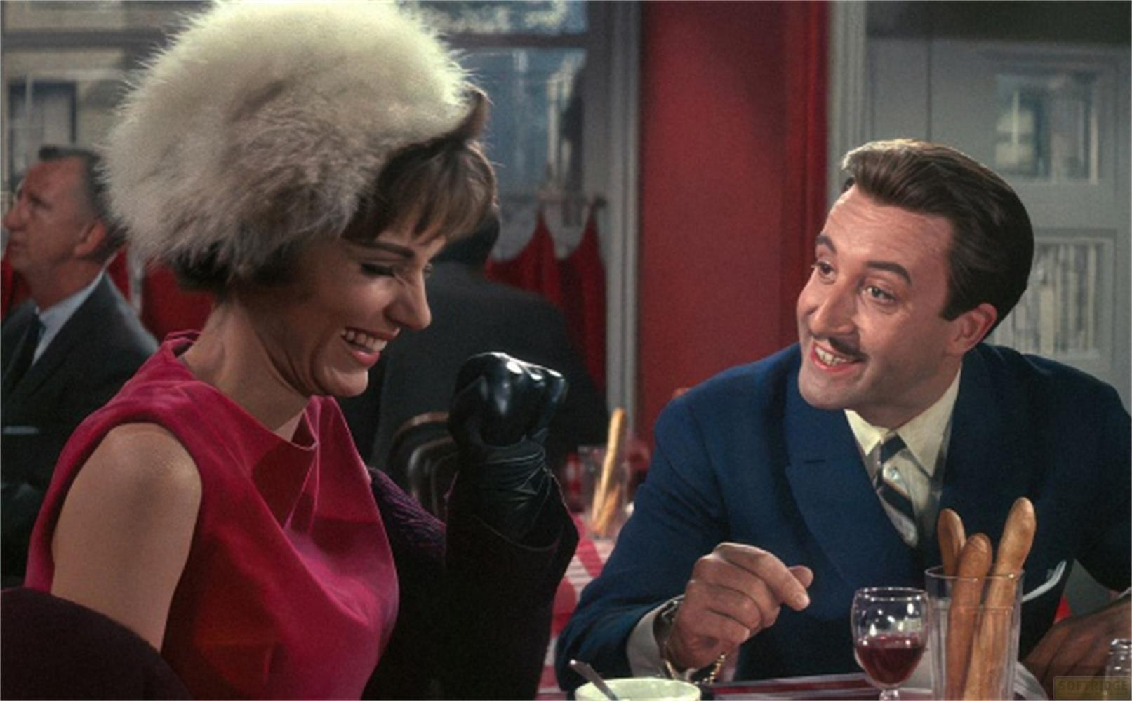 Un uomo e una donna seduti a un tavolo. Lei indossa un cappello di pelliccia e un vestito rosso.