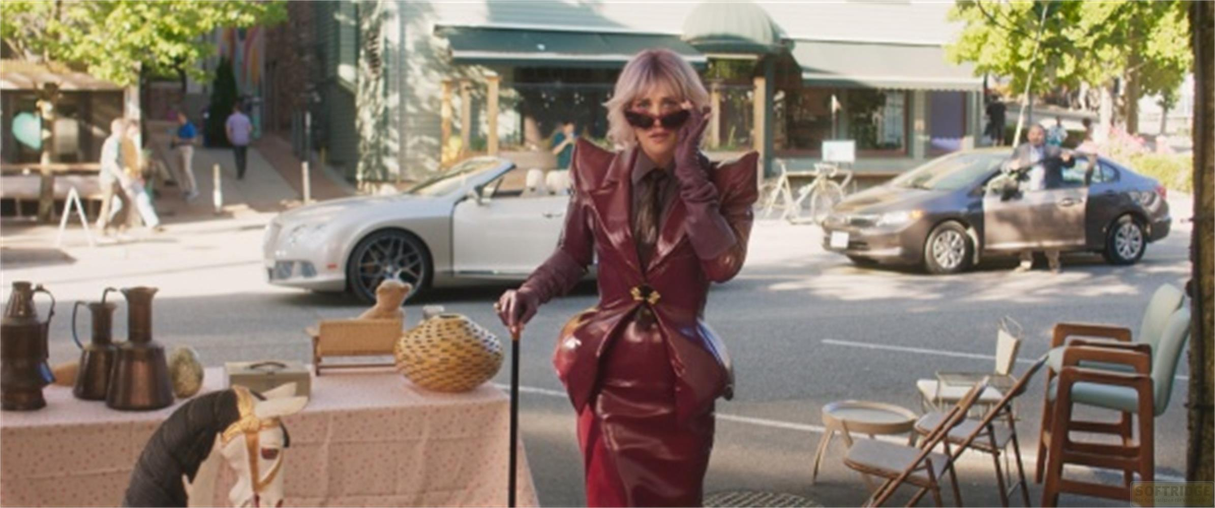 Una donna in un outfit di vernice rossa sta con un bastone per strada. Auto e bancarella sul retro.