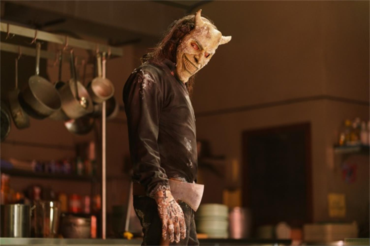 Un uomo con maschera demoniaca e corna, con un'ascia, si trova in una cucina.