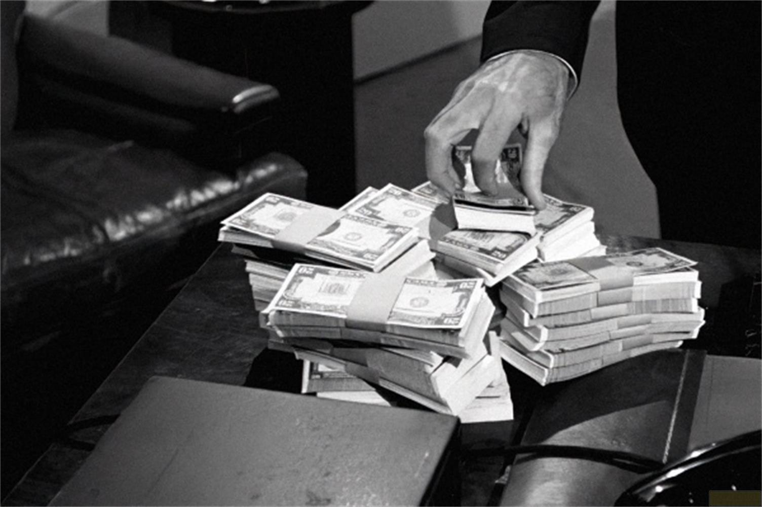 Un uomo conta pacchi di soldi su un tavolo. Tiene un piccolo pacco in mano.