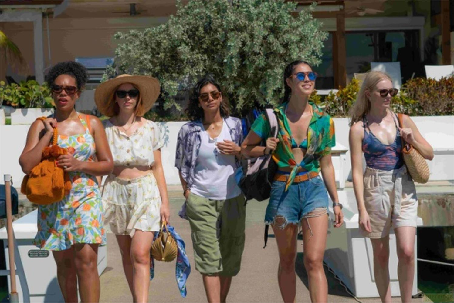 Cinque donne in abiti estivi camminano all'aperto. Alberi ed edifici sullo sfondo.