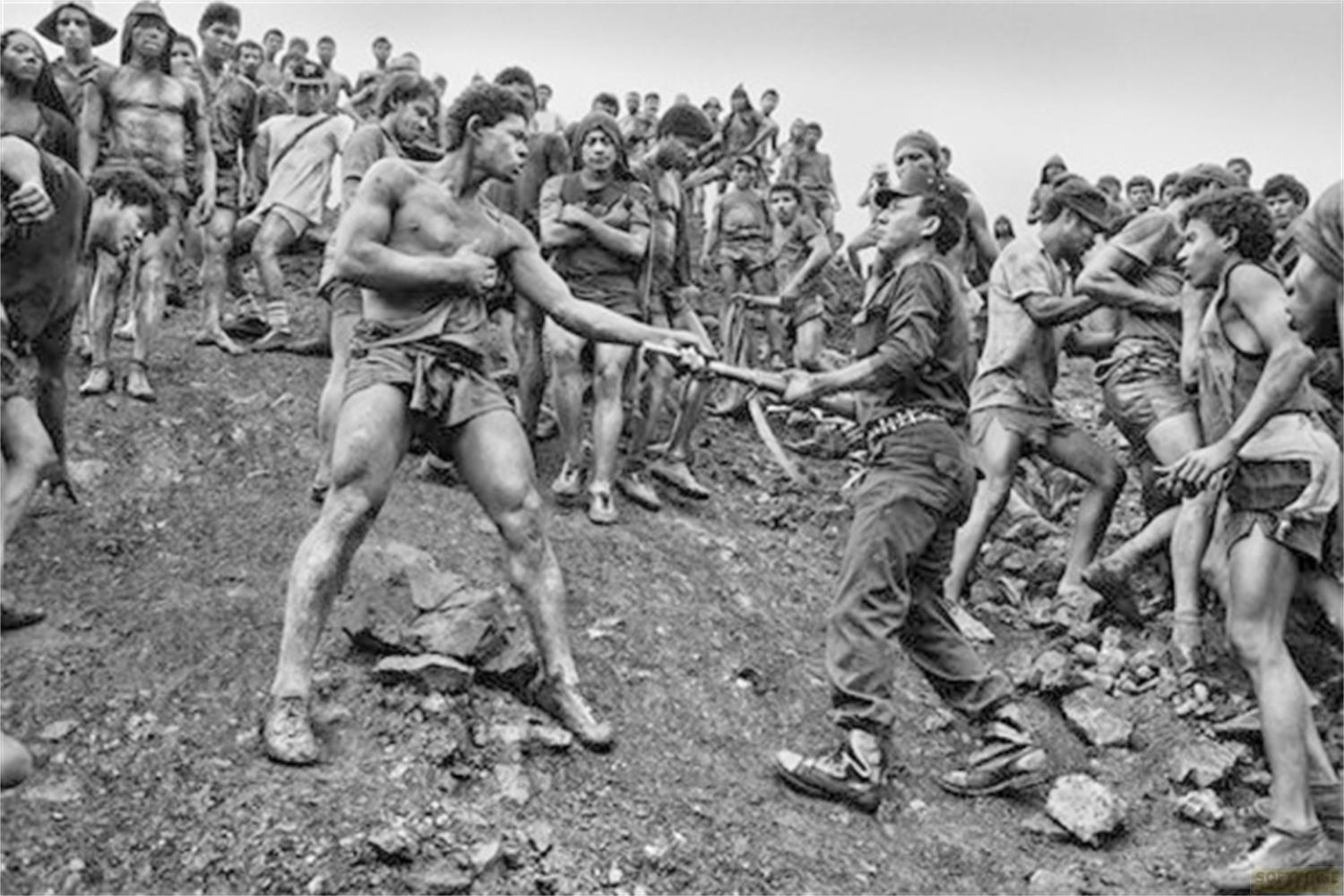 Uomini combattono con attrezzi in un campo pieno di gente.