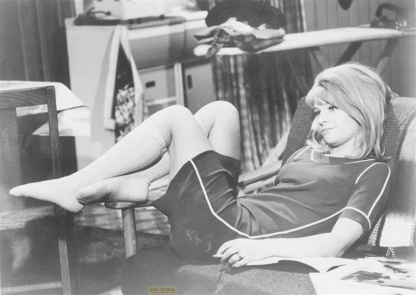 Una donna bionda seduta su una poltrona con le gambe accavallate e appoggiate.