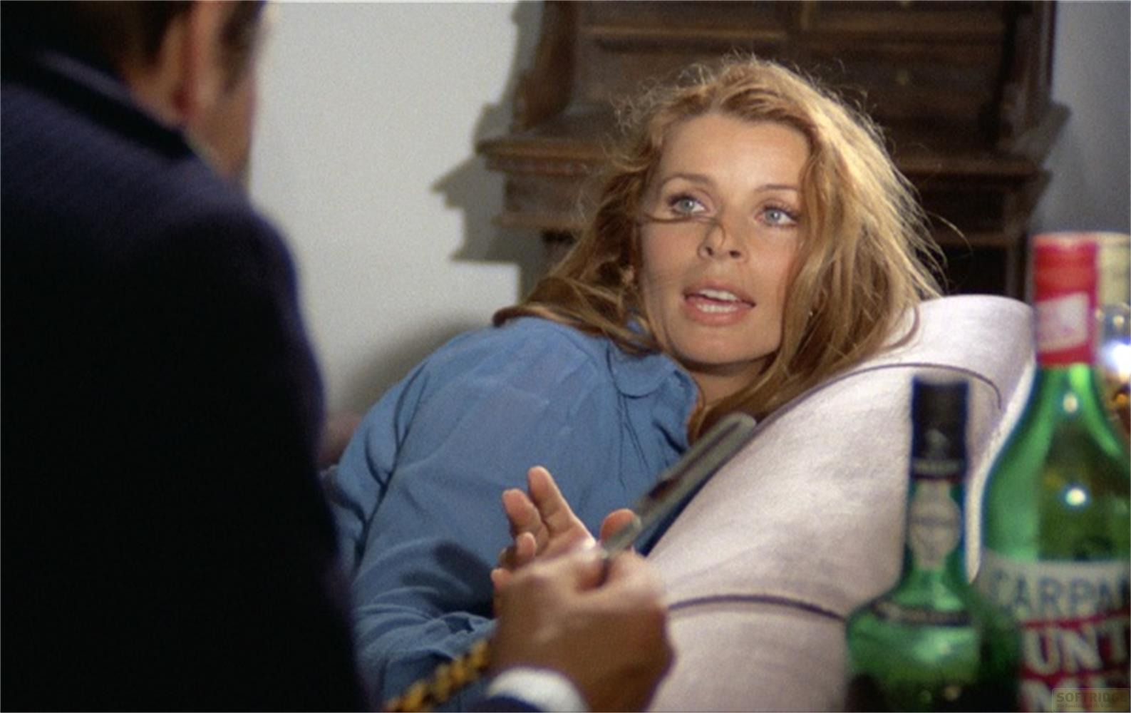 Una donna bionda in camicia blu giace su un cuscino. Si vedono due bottiglie.