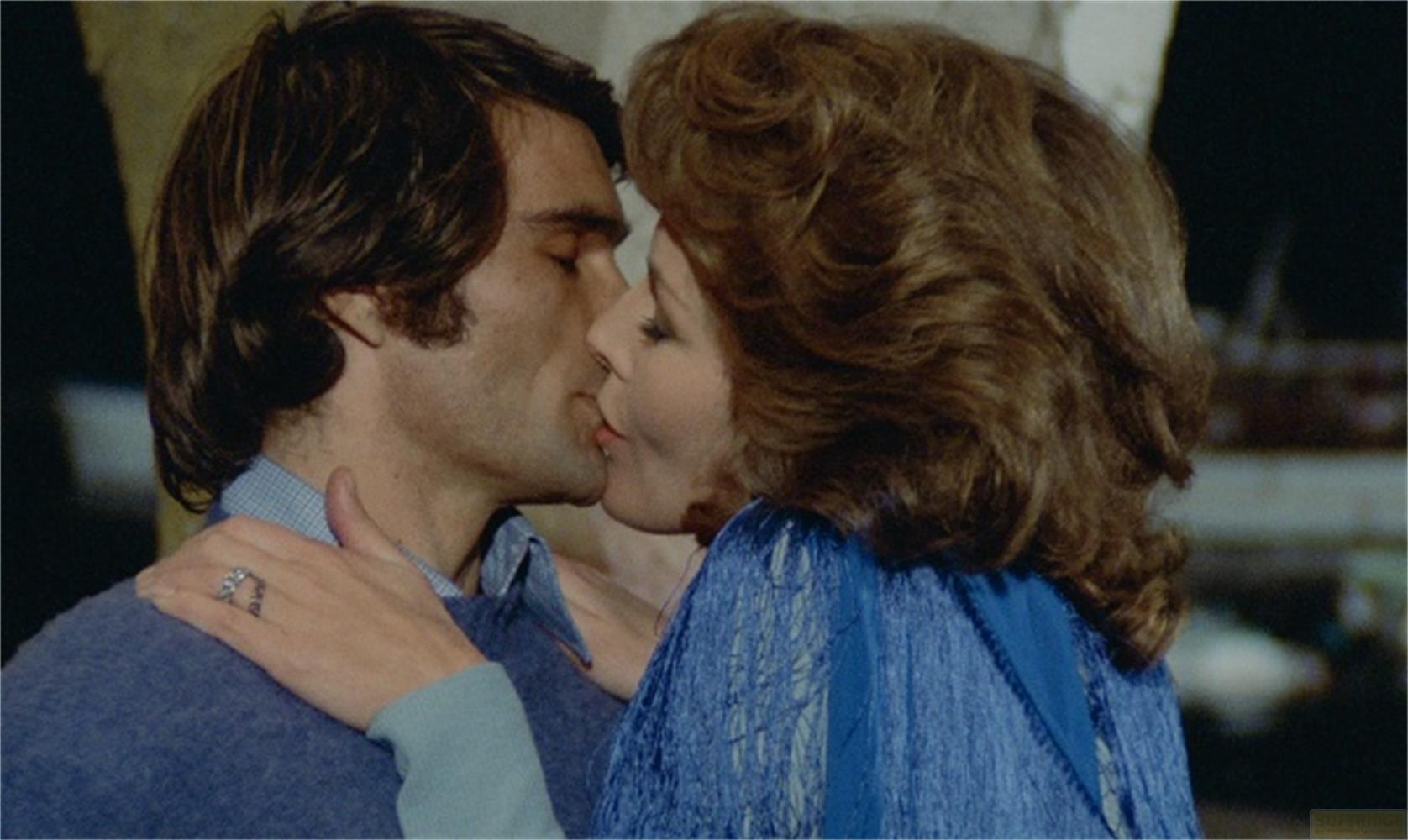 Un uomo e una donna si baciano. Lei indossa un vestito blu.