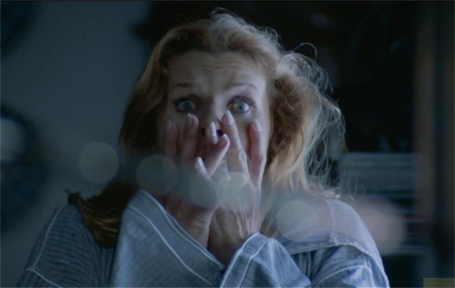 Una donna con gli occhi spalancati e la bocca aperta, mani davanti al viso.