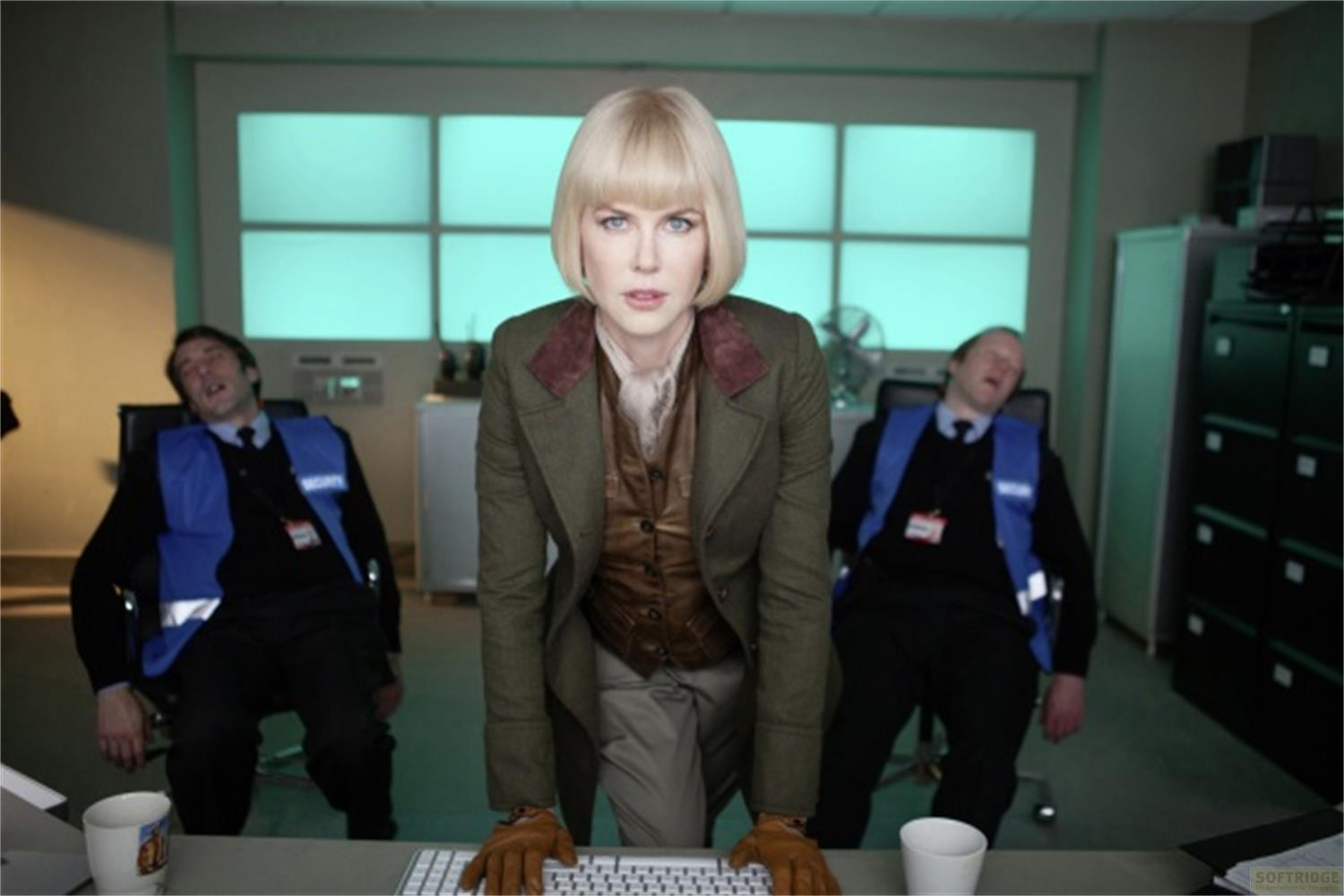 Una donna in verde si erge davanti a due uomini addormentati in gilet blu.