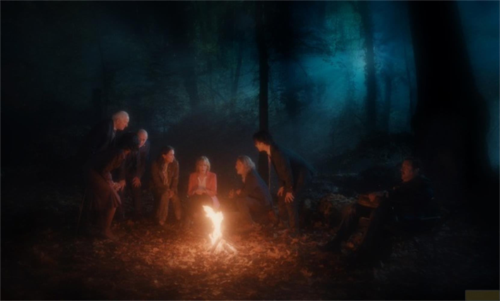 Gruppo di persone sedute attorno a un falò in una foresta oscura.