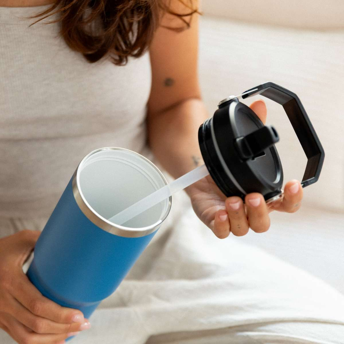 Una persona sostiene un vaso azul y una tapa negra con pajita.