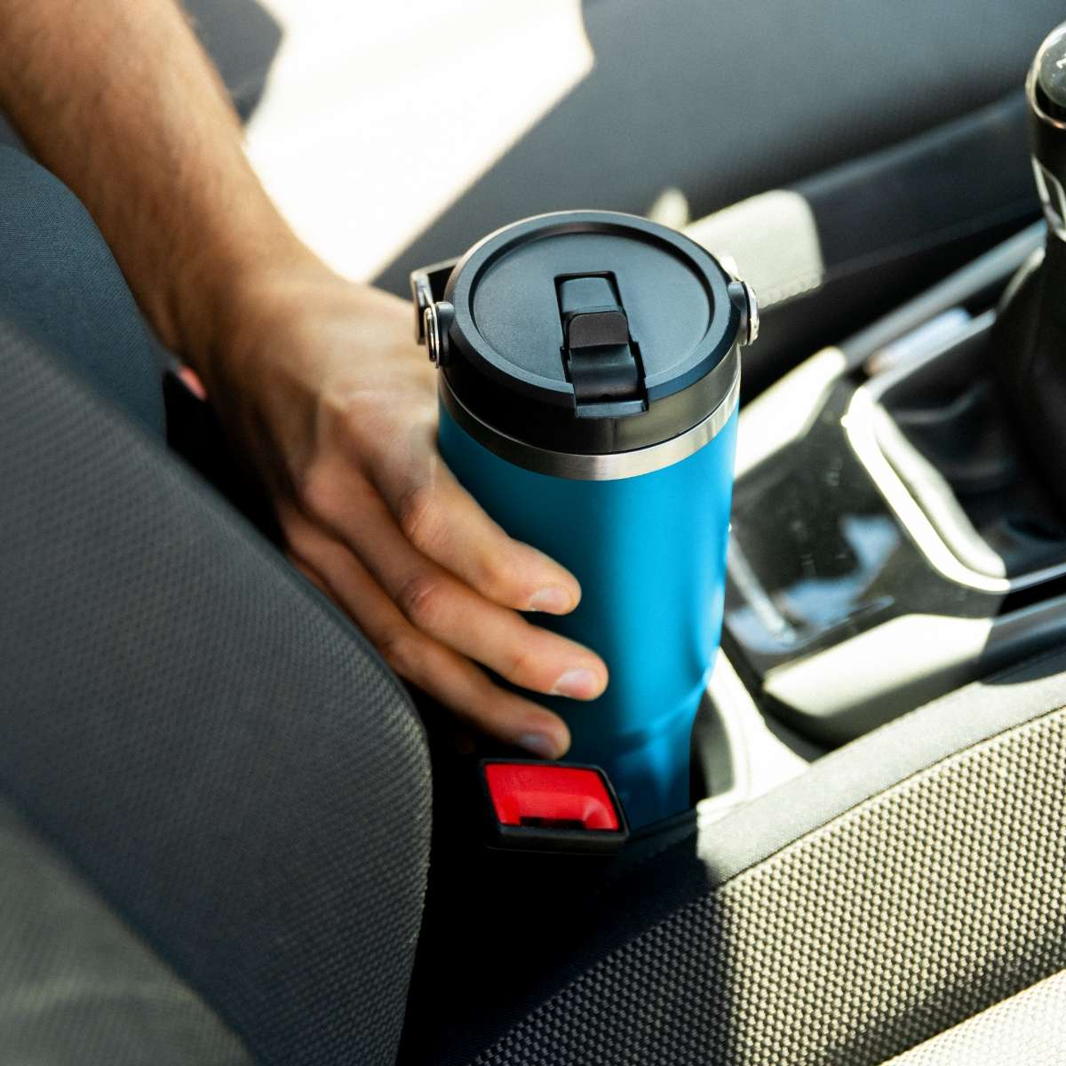 Termo azul en un portavasos de coche, sostenido por una mano.