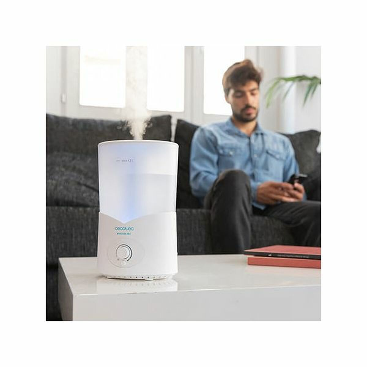 Mężczyzna siedzi na kanapie, patrząc na telefon, podczas gdy nawilżacz wypuszcza parę.