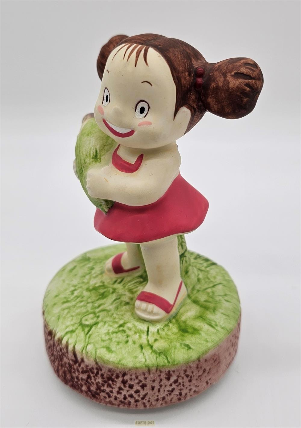 Eine Figur eines Mädchens mit Zöpfen, das ein grünes Objekt hält.