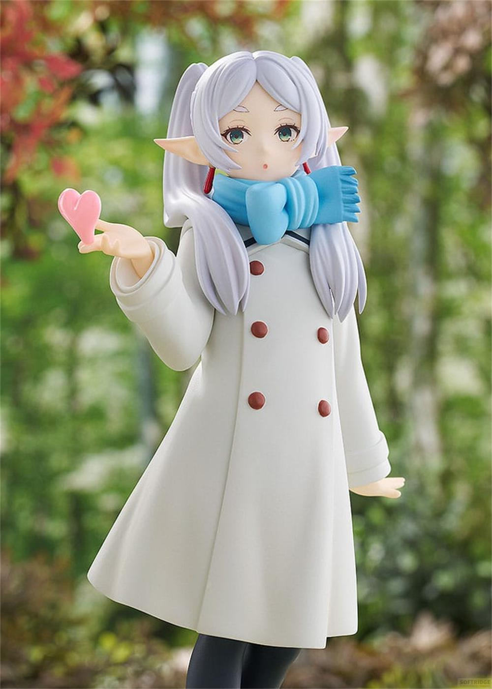 Figura con abrigo blanco, bufanda azul y corazón rosa. Al aire libre.