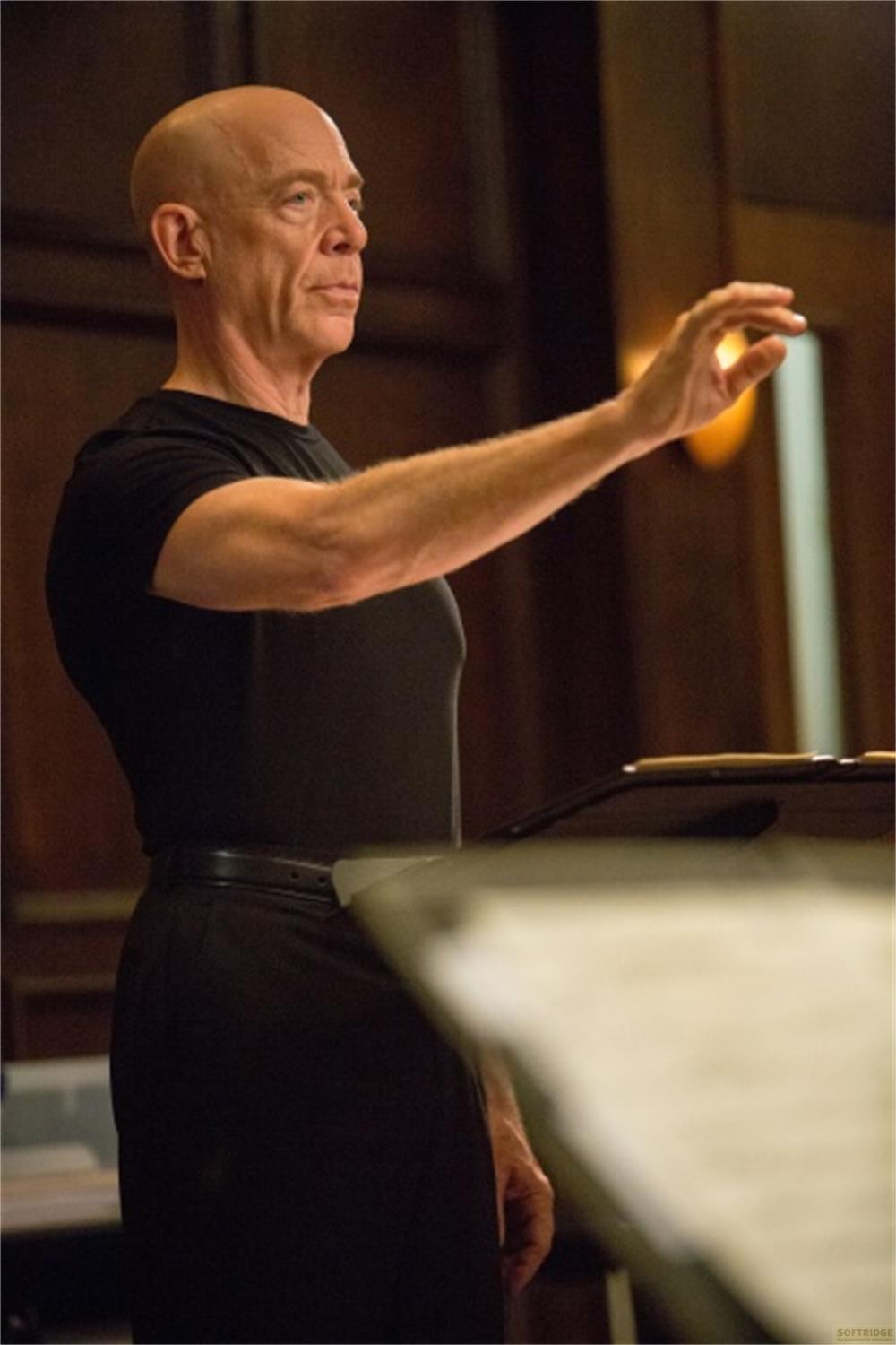 Un homme chauve en chemise noire lève la main dans une fosse d'orchestre.