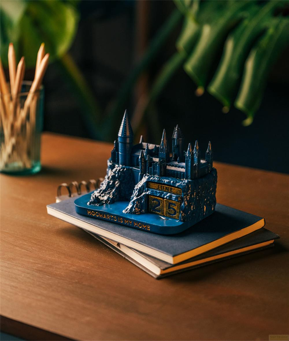 Una figura del castillo azul de Hogwarts con calendario sobre libros en mesa.