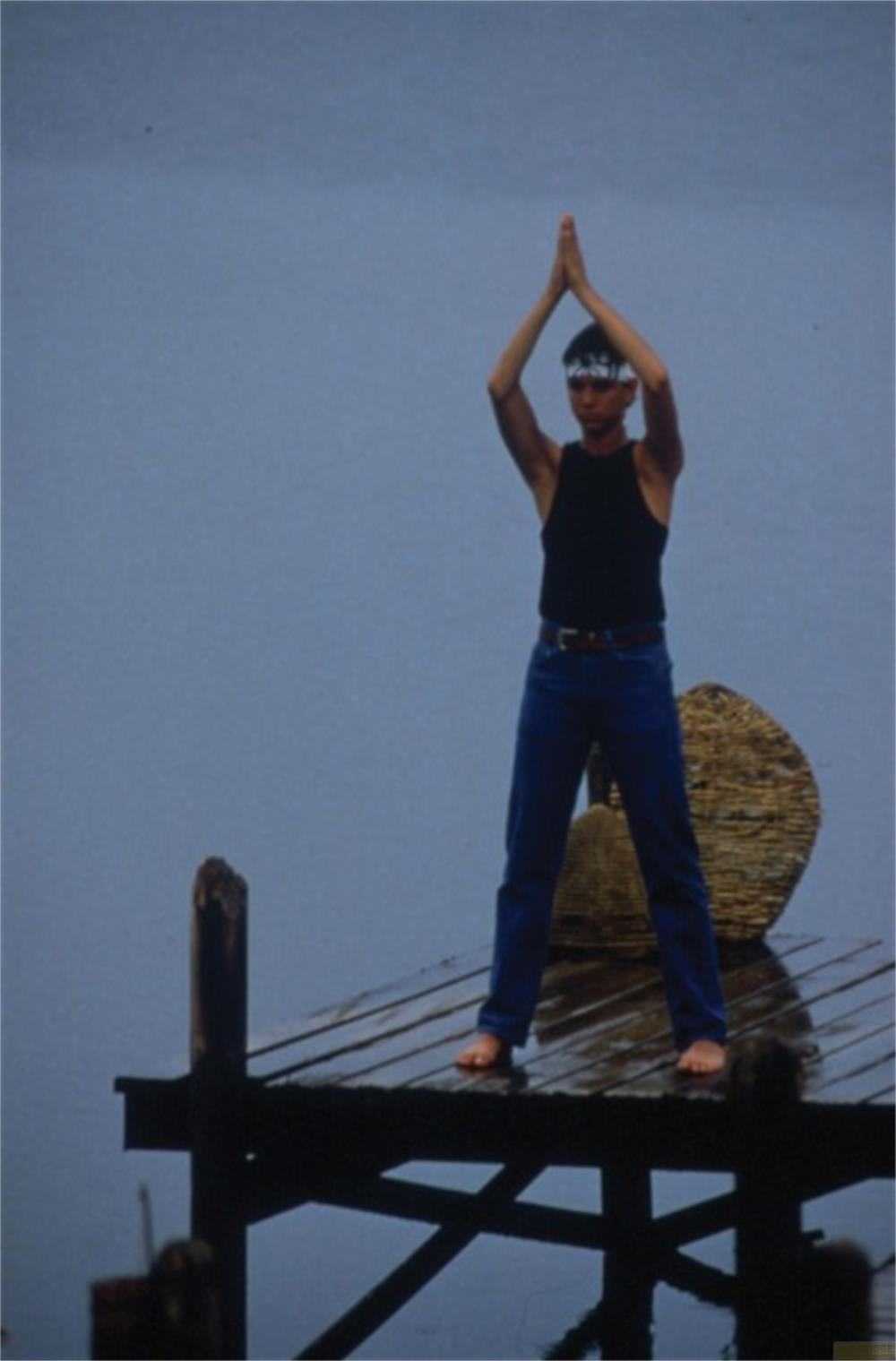 Homme sur une jetée en bois, mains levées, bandeau sur la tête.