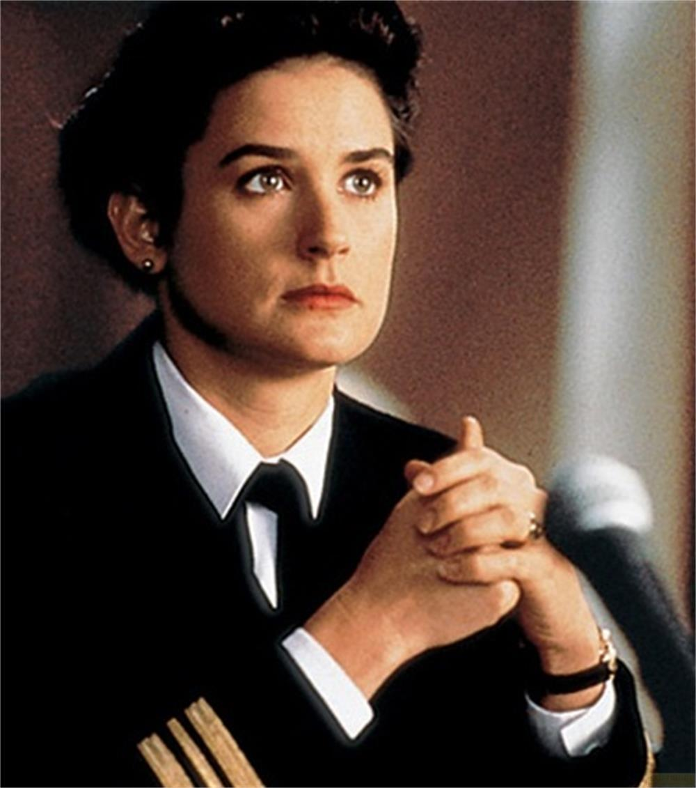Femme en costume bleu marine, chemise blanche et cravate, mains jointes.