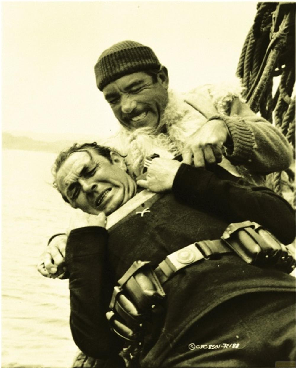 Un homme barbu étrangle un autre homme en costume sombre sur un bateau