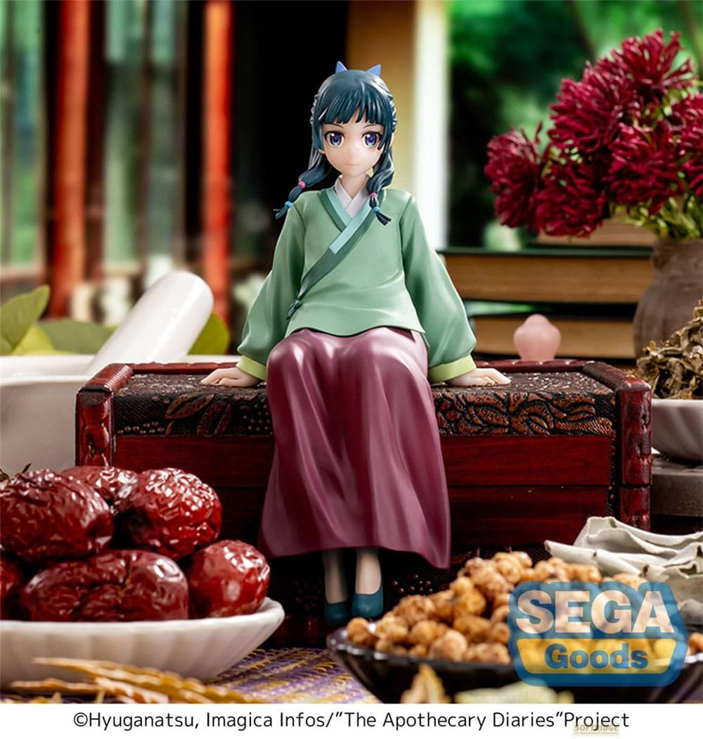 Figurine d'une fille en tenue traditionnelle, assise sur un coffre, avec fruits et fleurs.