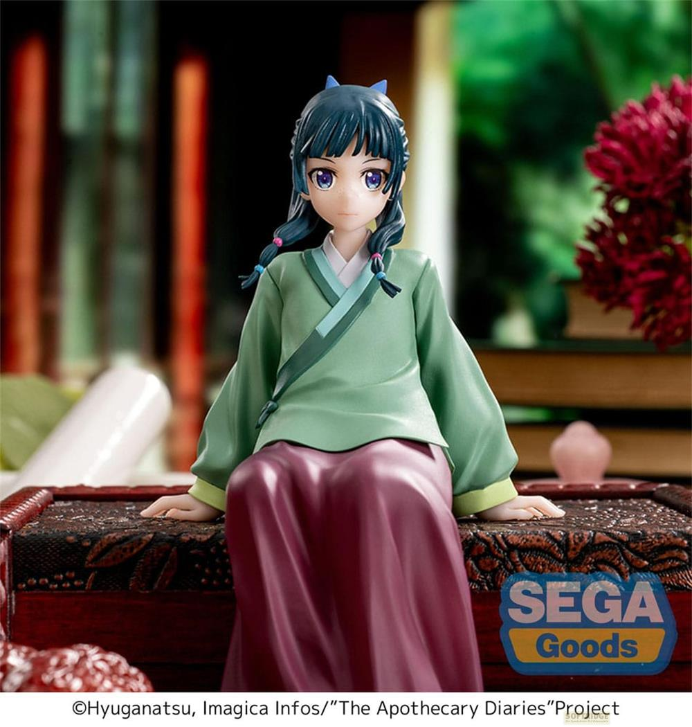 Figurine d'anime en robe verte et jupe violette, assise sur un coffre.
