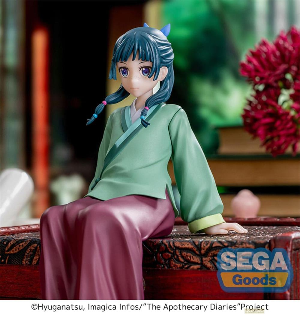 Une figurine en kimono vert et jupe violette assise sur un coffre.