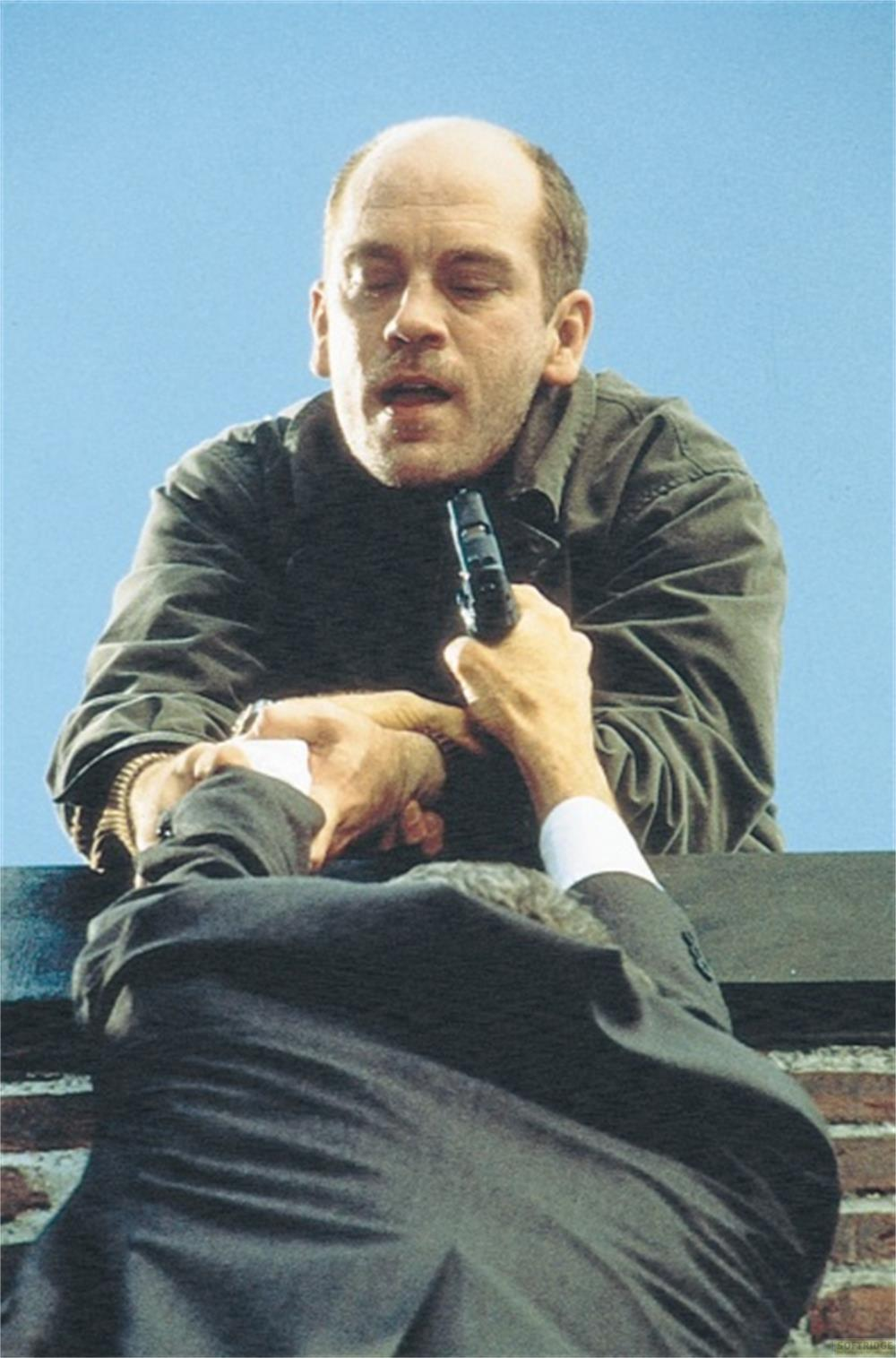 Un homme armé menace un autre homme sur un toit.