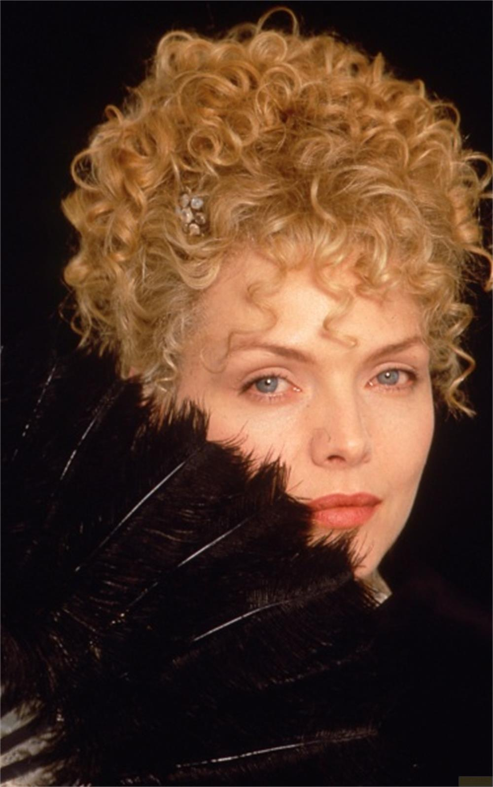 Femme aux cheveux blonds bouclés et éventail en plumes noires sur fond sombre.