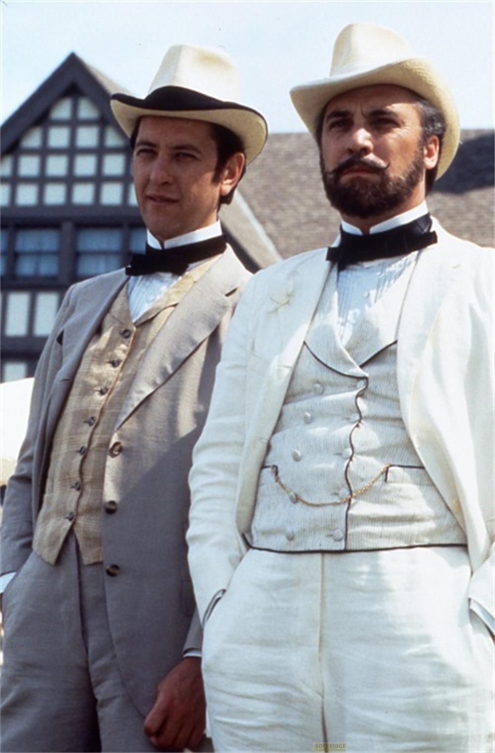 Deux hommes en costume et chapeau se tiennent devant un bâtiment.