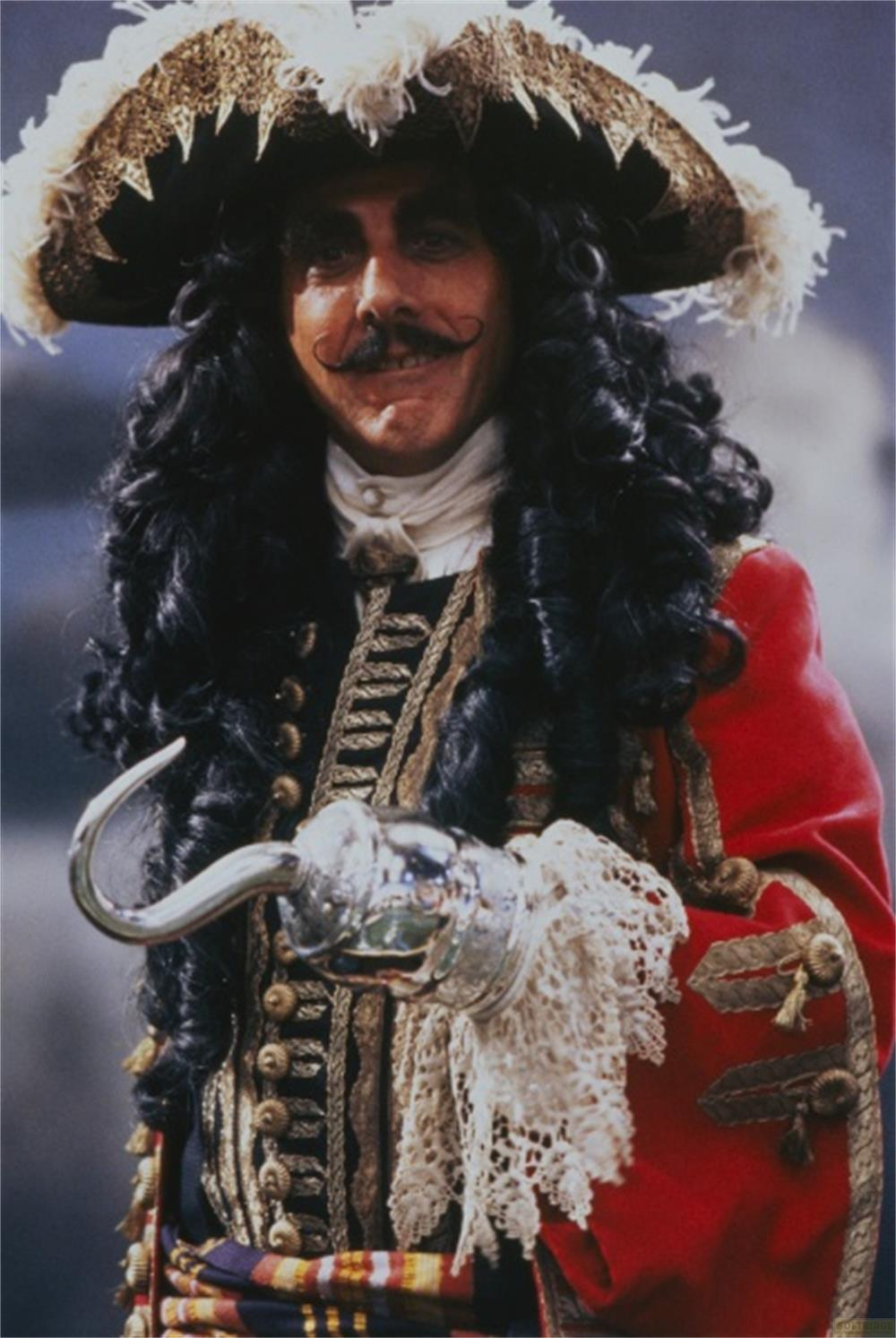 Un homme avec une main en crochet, des cheveux noirs et un chapeau de pirate porte des vêtements rouges.