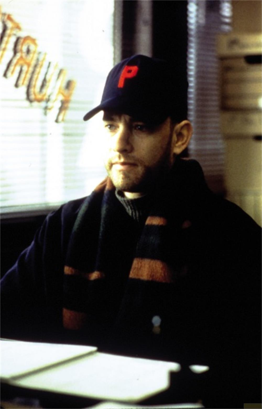 Homme portant une casquette rouge 'P' et une écharpe devant une fenêtre.