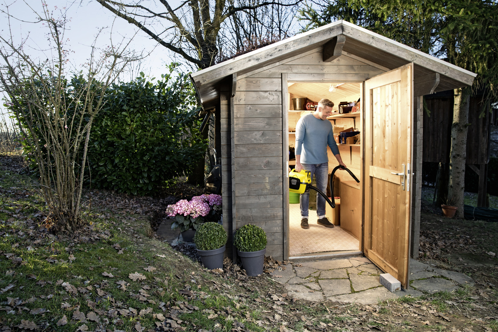 Man with yellow vacuum cleaner inside a wooden shed.