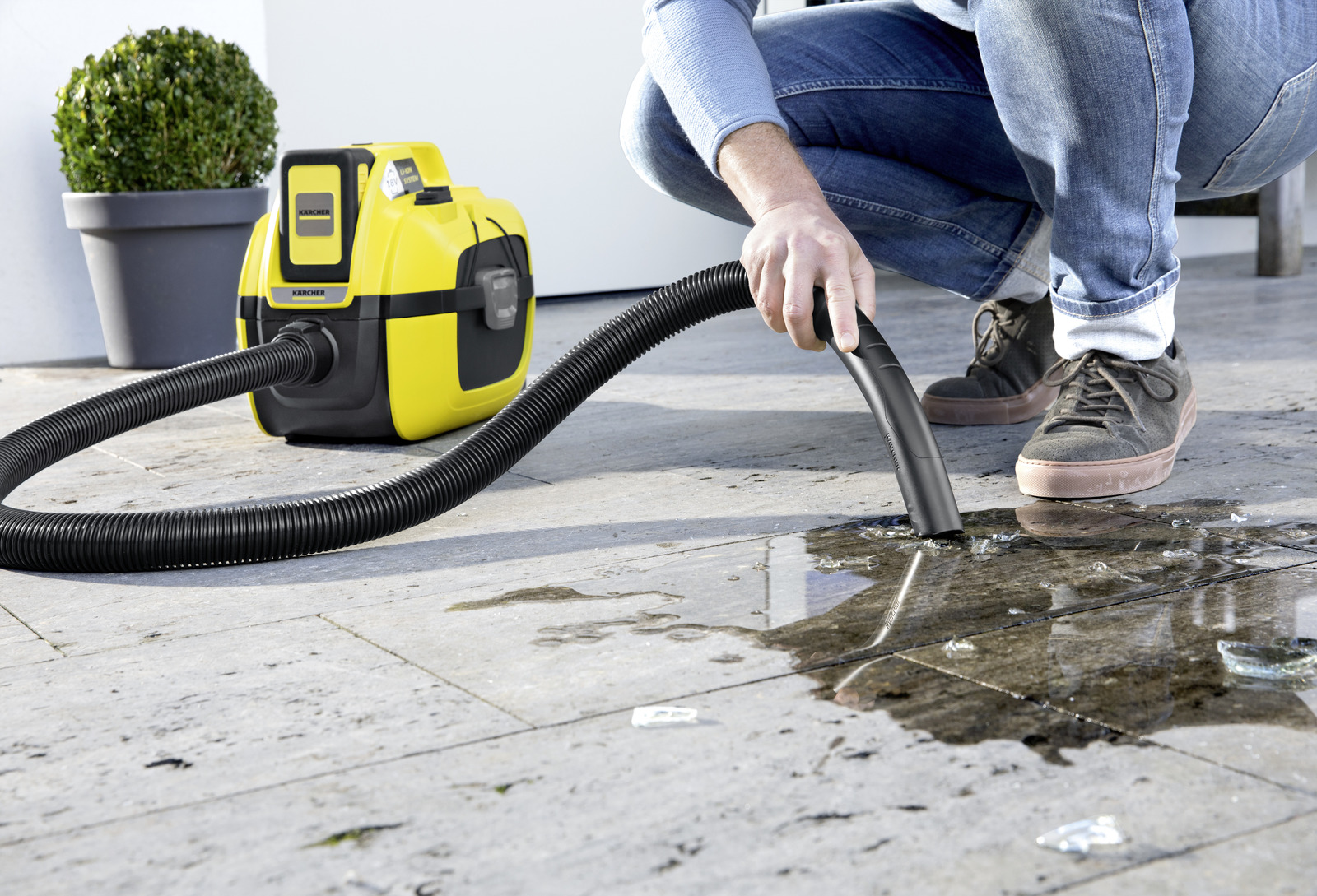 Man vacuums water with a yellow Karcher wet/dry vacuum cleaner.