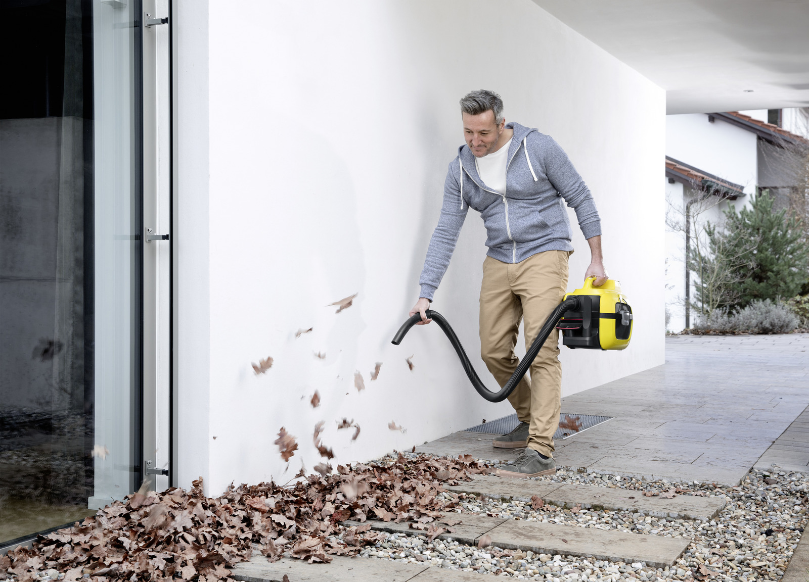 Man vacuums leaves against a white wall with a yellow vacuum