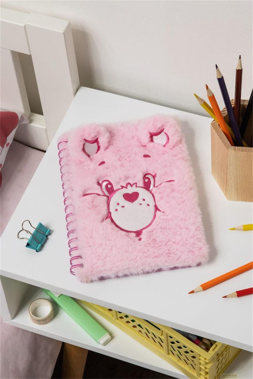 Ein flauschiges rosa Notizbuch mit Bärengesicht auf einem Nachttisch.