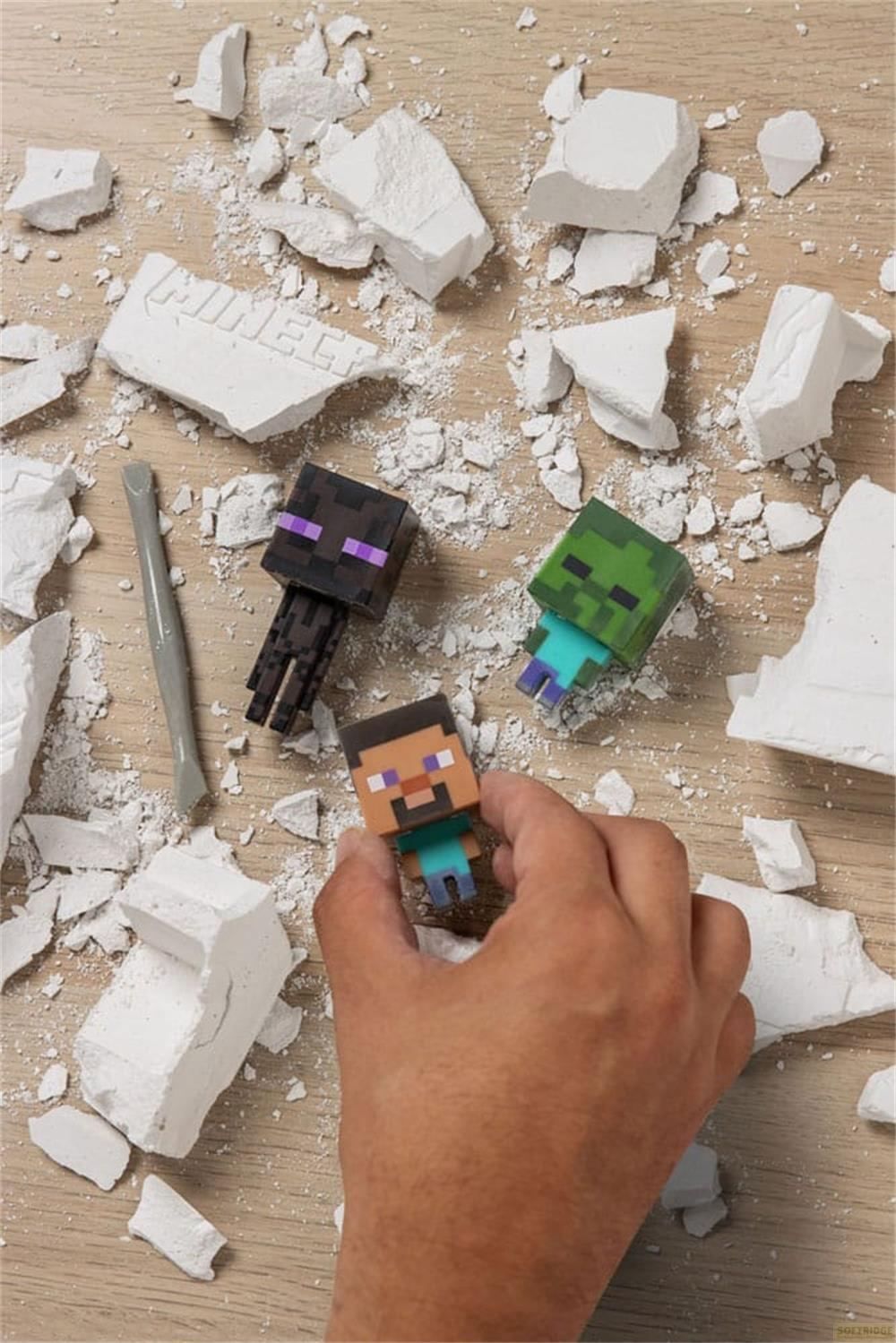Hand hält Minecraft Steve Figur neben Zombie und Enderman, von Gipsstücken umgeben.