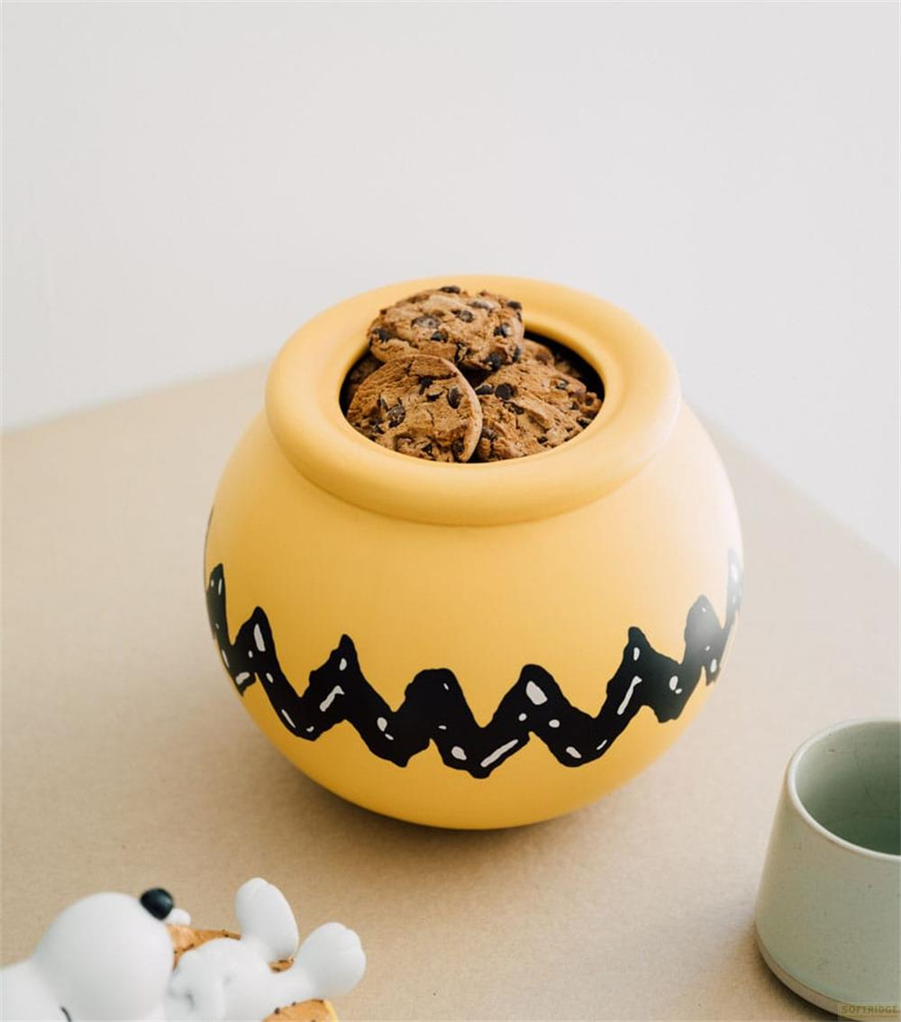 Un tarro amarillo con galletas y patrón de zigzag negro. Un perro y taza cerca.