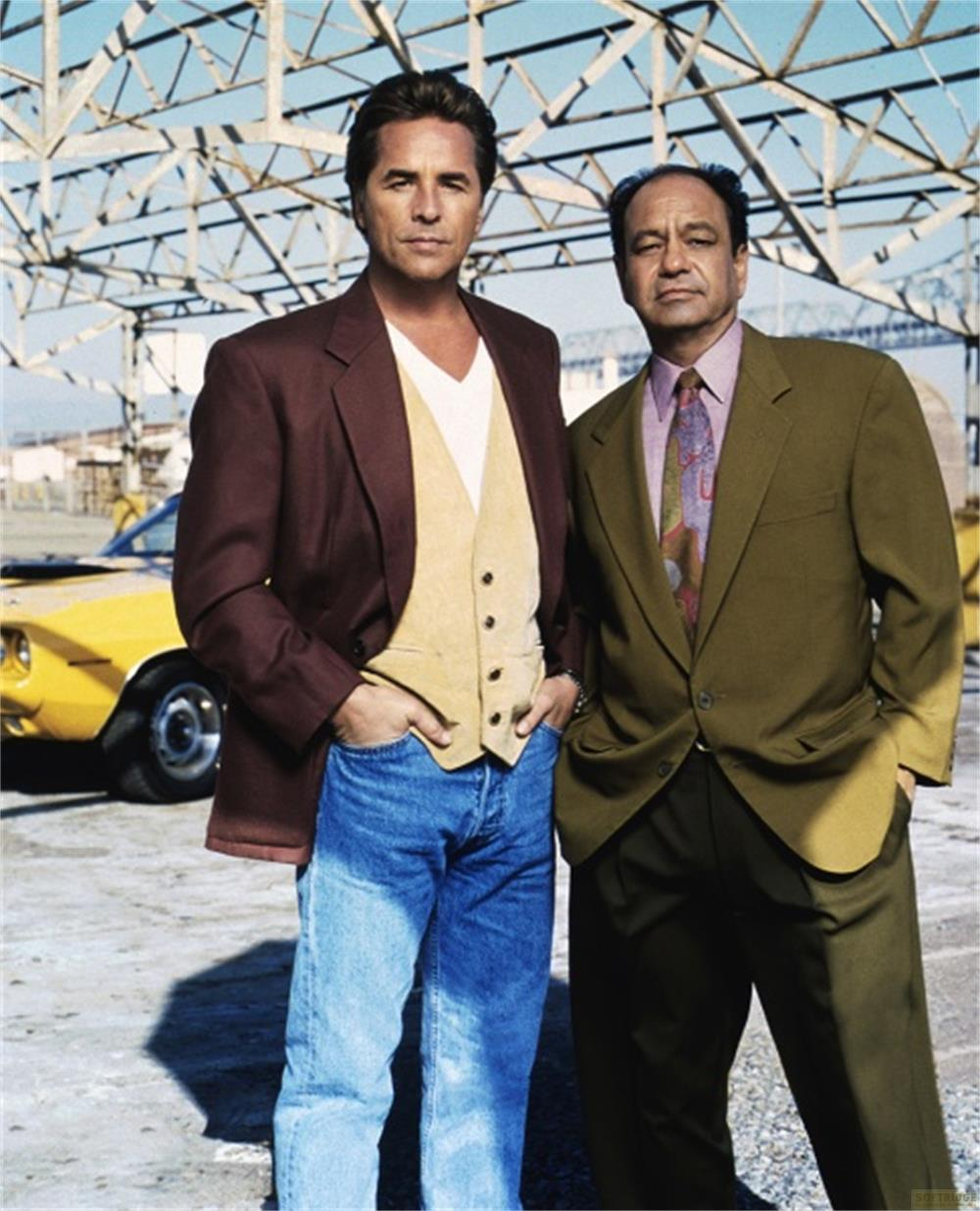 Deux hommes debout devant une voiture classique jaune et une structure métallique.