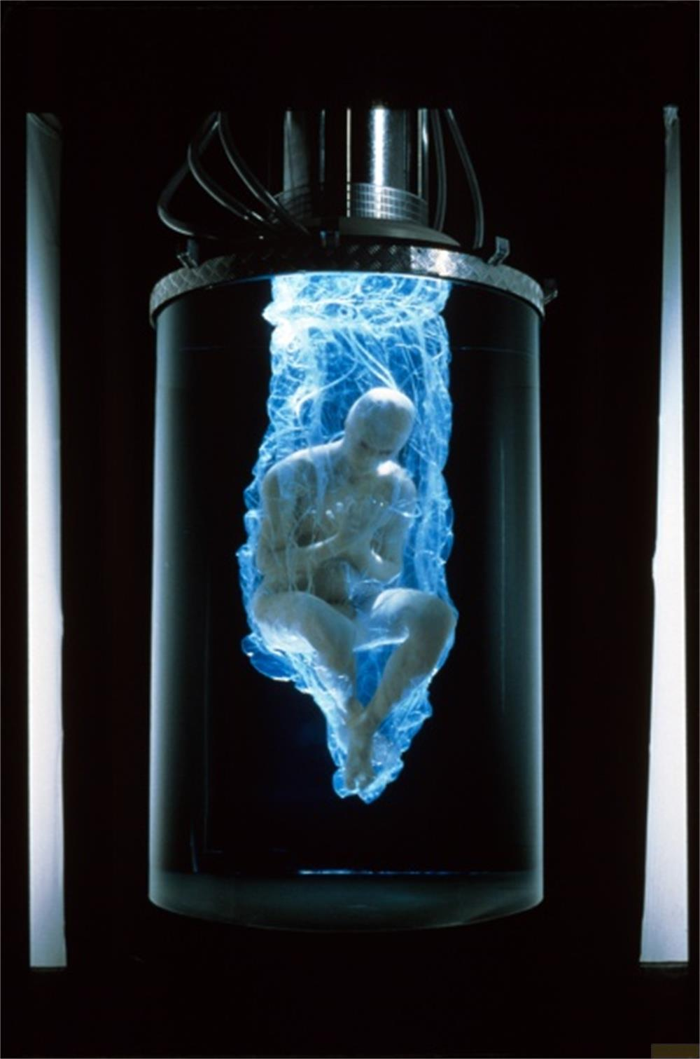 Une figure humaine dans un cocon bleu lumineux dans un récipient cylindrique.