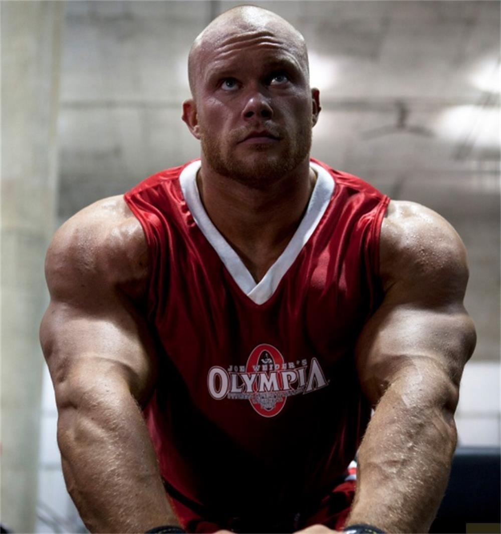 Ein muskulöser Mann mit Glatze und Bart in einem roten Olympia-Shirt.