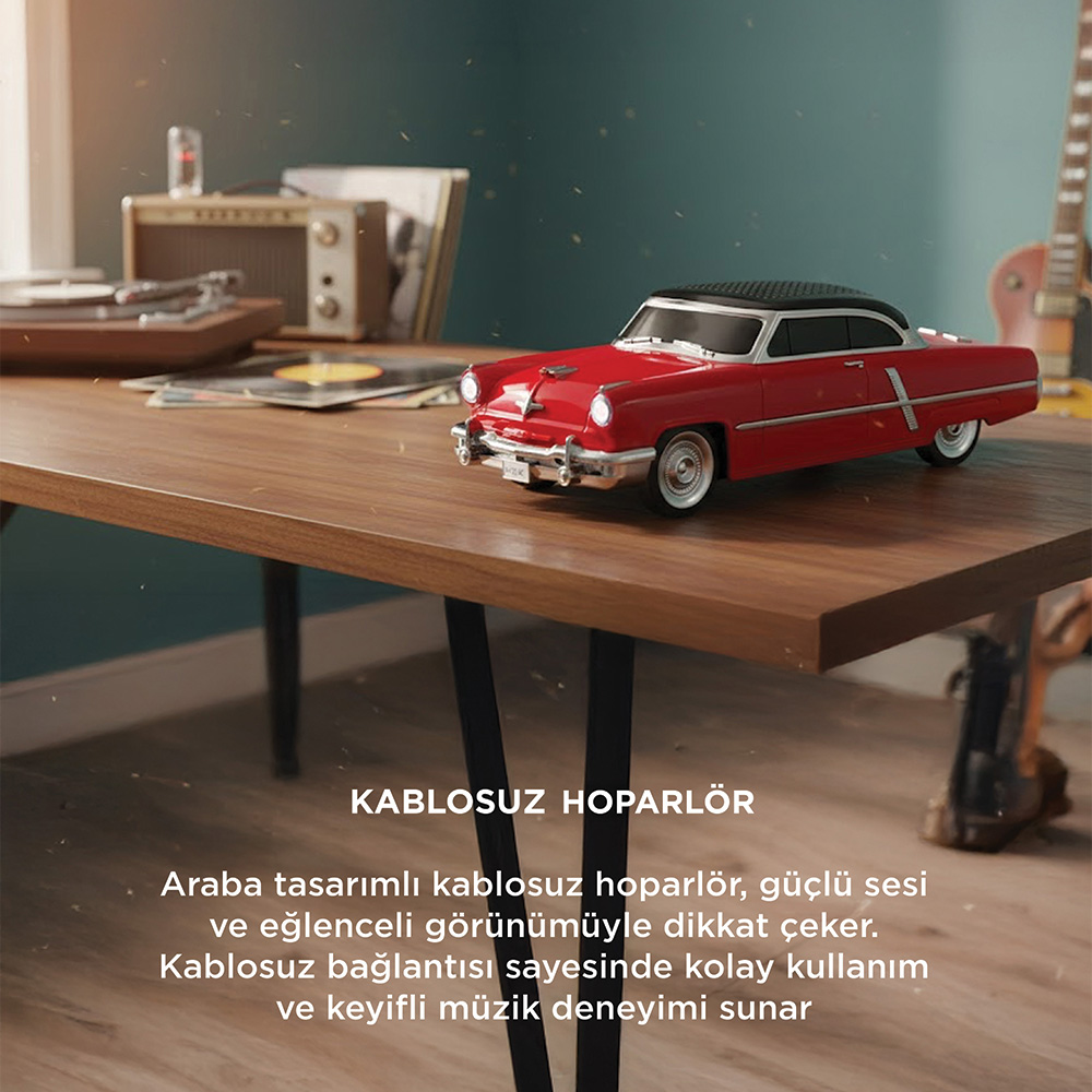 Kırmızı bir araba hoparlör modeli, plakların yanında ahşap bir masada duruyor.