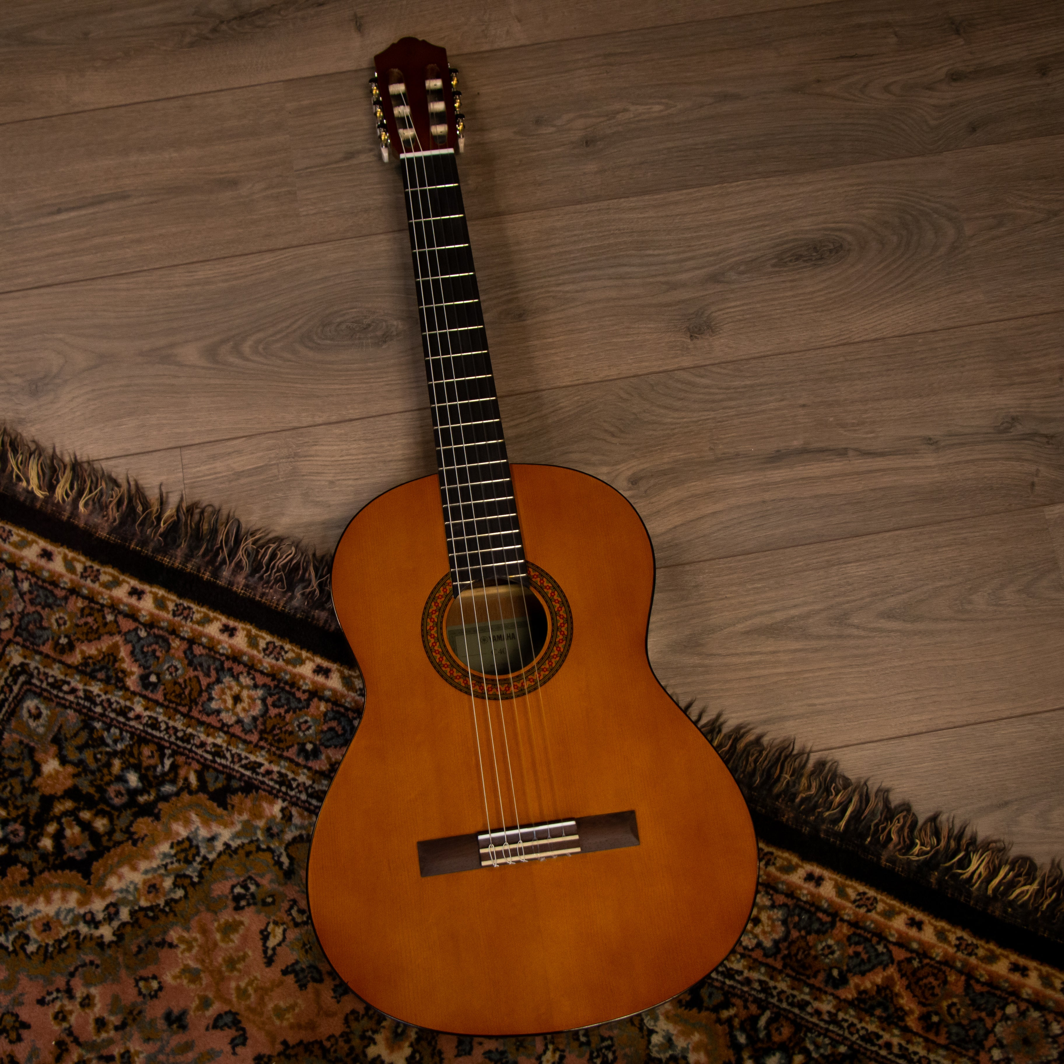 Eine Gitarre liegt auf einem Holzboden neben einem gemusterten Teppich.