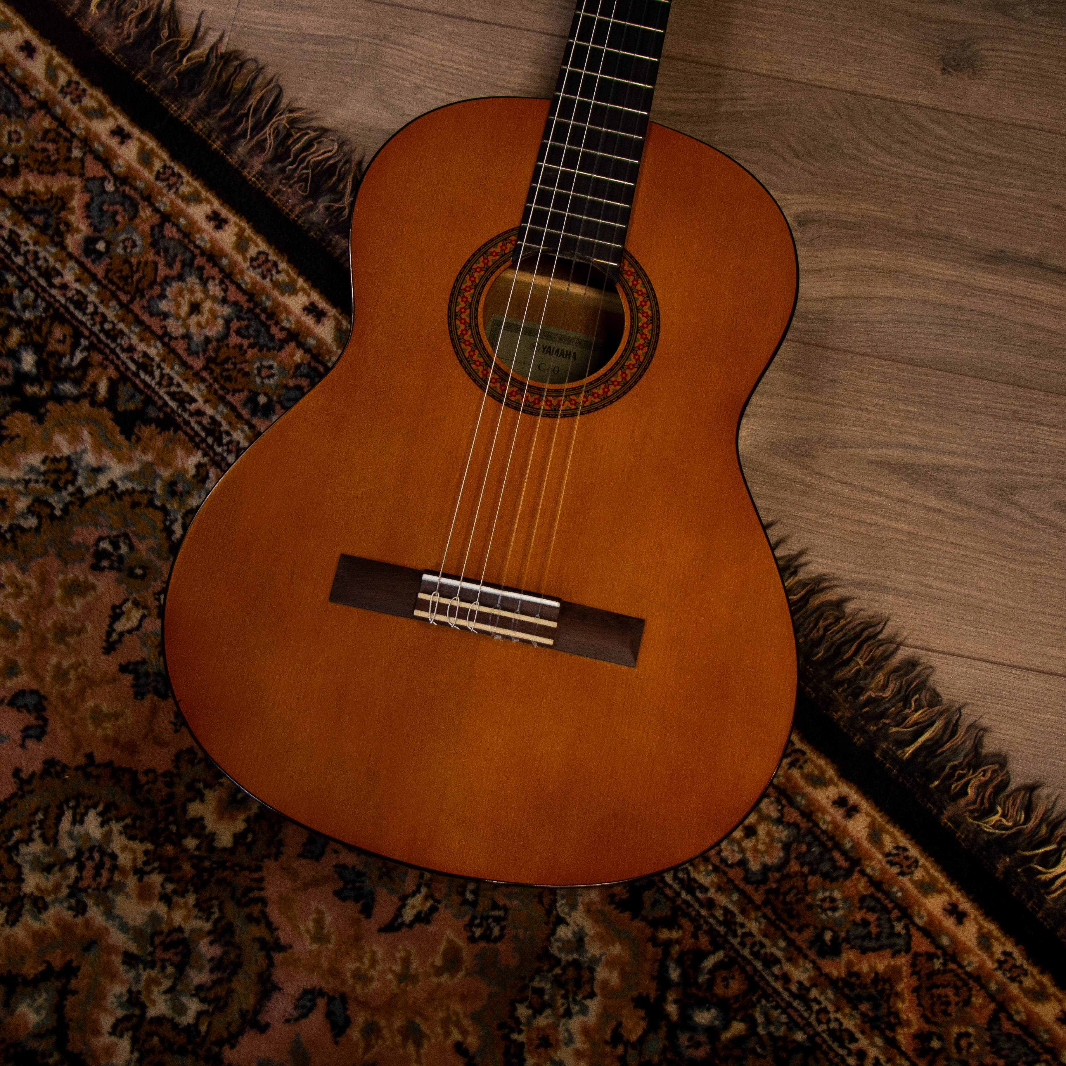 Eine braune Gitarre liegt auf einem gemusterten Teppich und Holzboden.