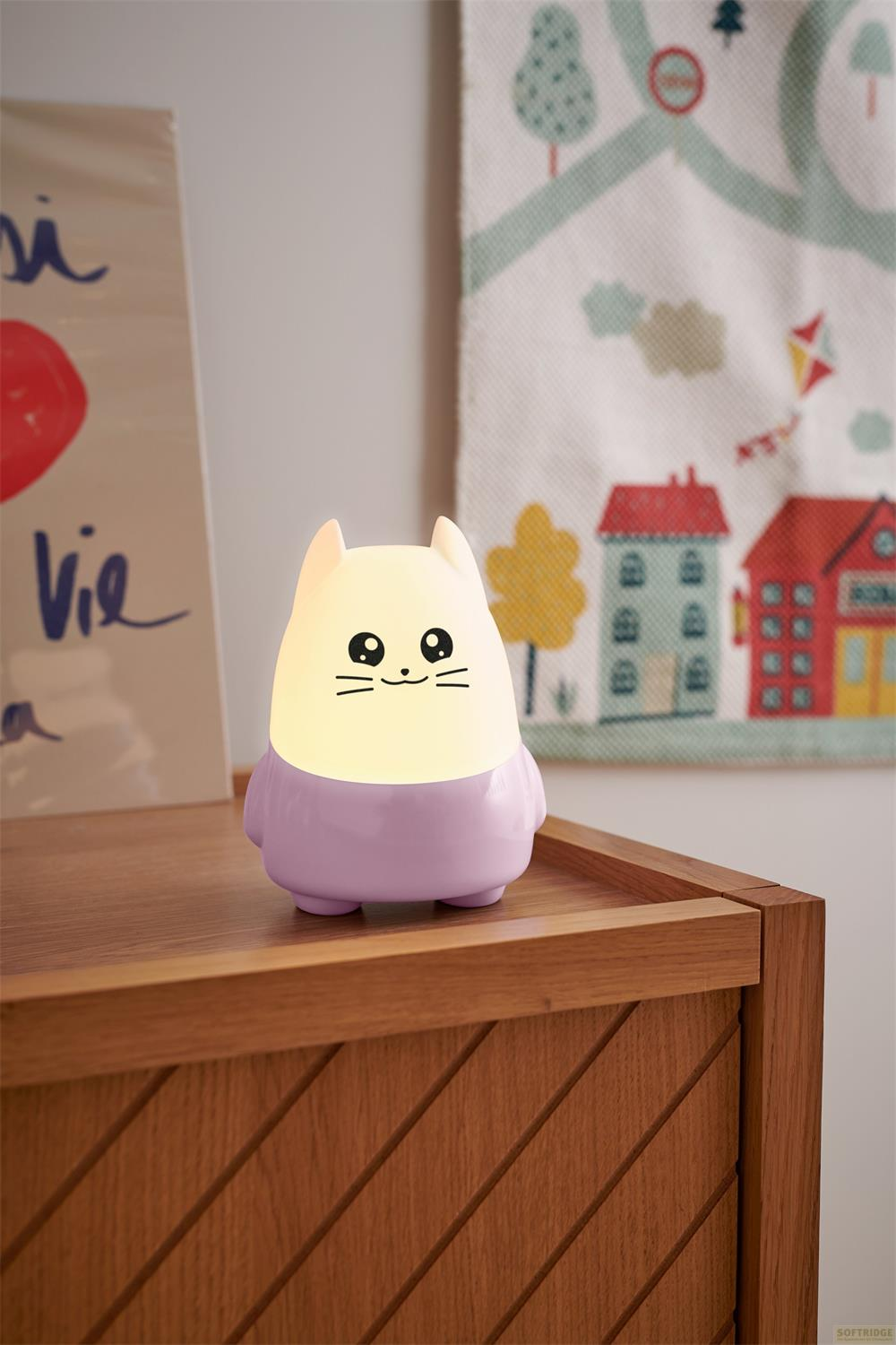 Une petite lampe chat lumineuse sur un meuble en bois, avec un dessin en arrière-plan.