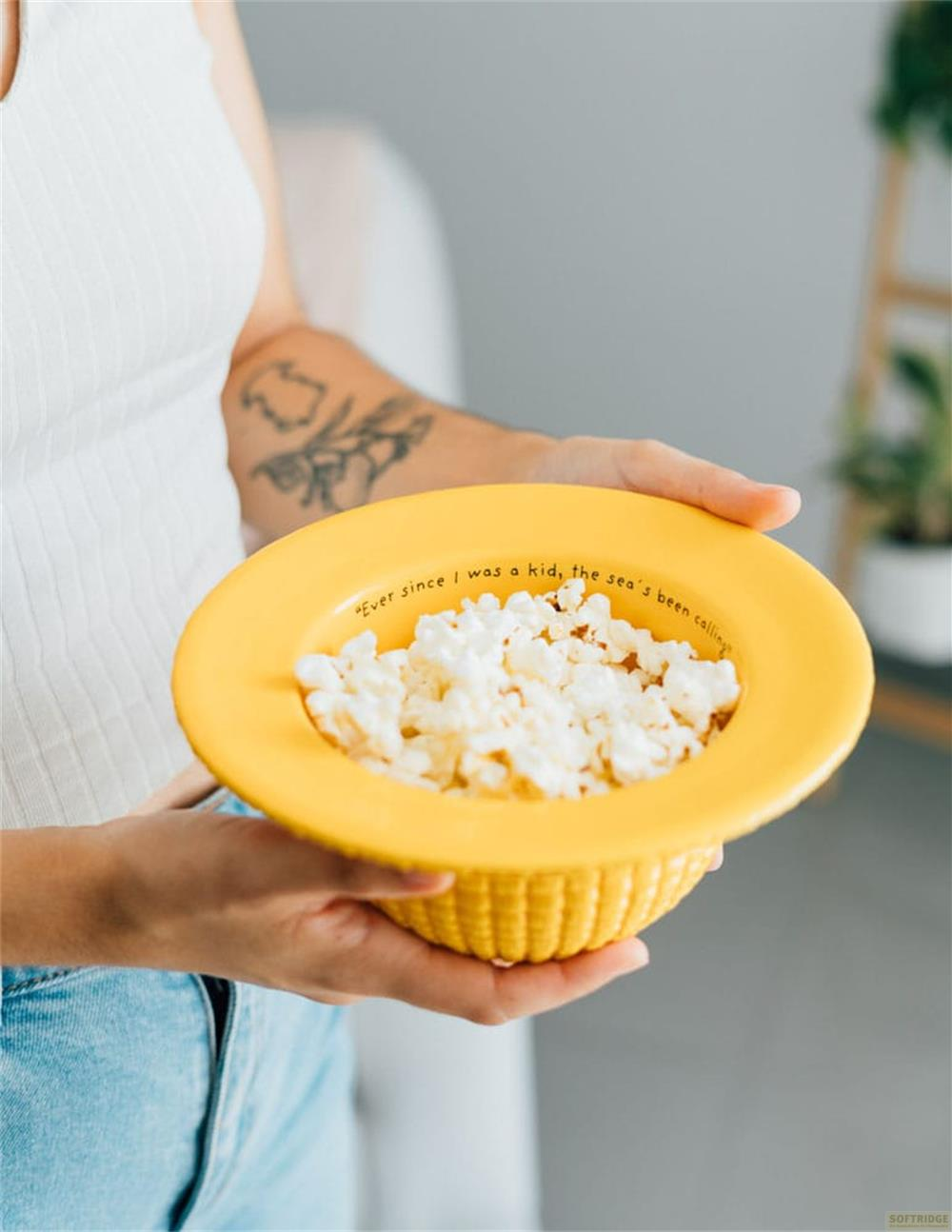 Una persona sostiene un cuenco amarillo lleno de palomitas de maíz. El cuenco tiene texto en el borde.