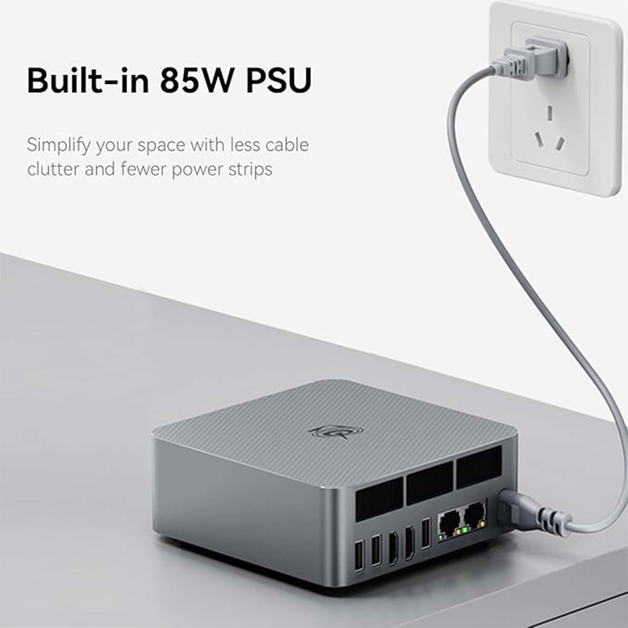 Szary mini PC z kablem zasilającym podłączonym do gniazdka ściennego.