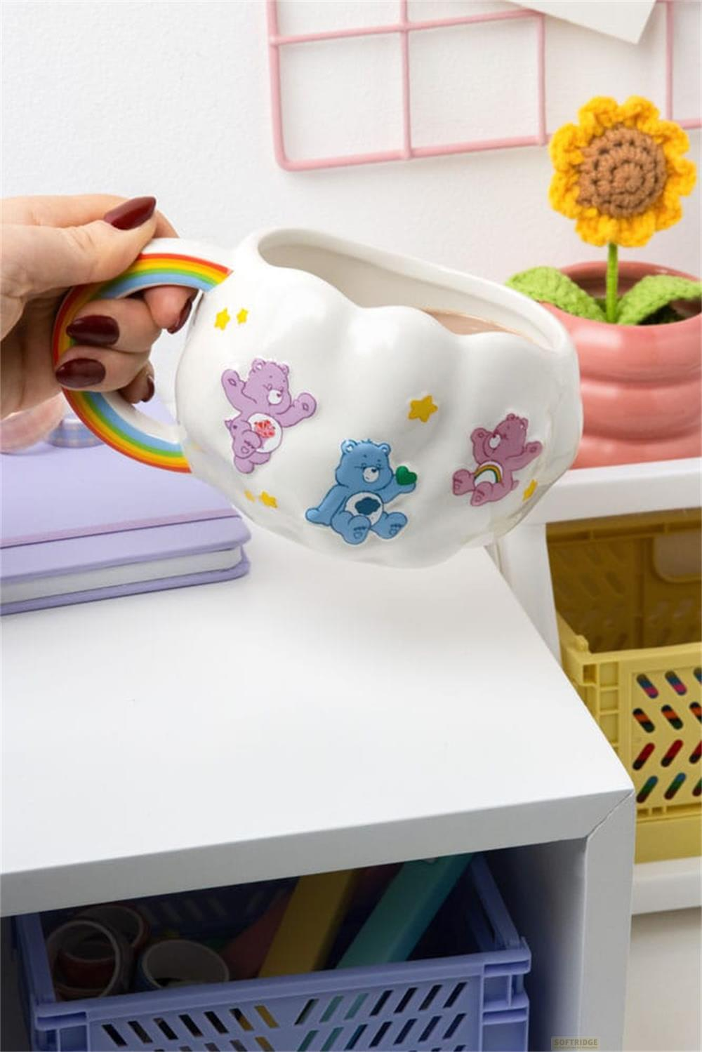 Taza blanca con forma de nube y asa de arcoíris, sostenida por una mano. Motivos de osos.