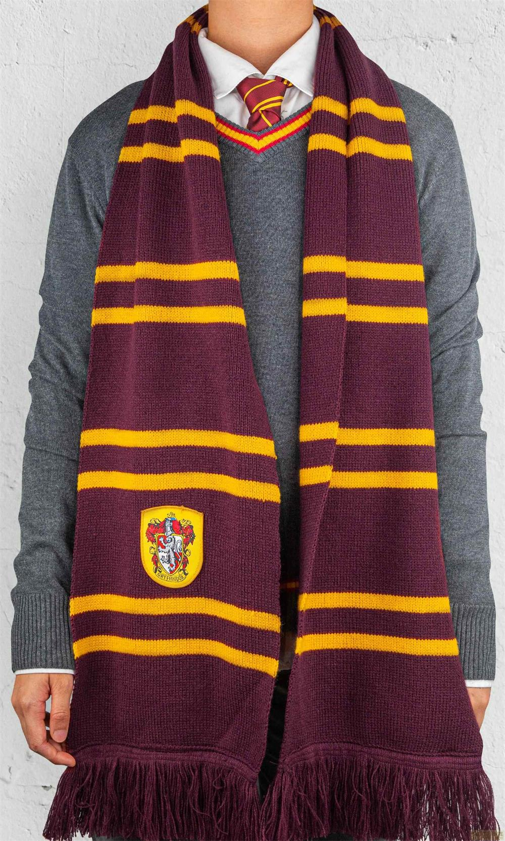 Ein Mann trägt einen grauen Pullover, weißes Hemd, Krawatte und einen Schal mit Streifen in Burgunderrot und Gelb.