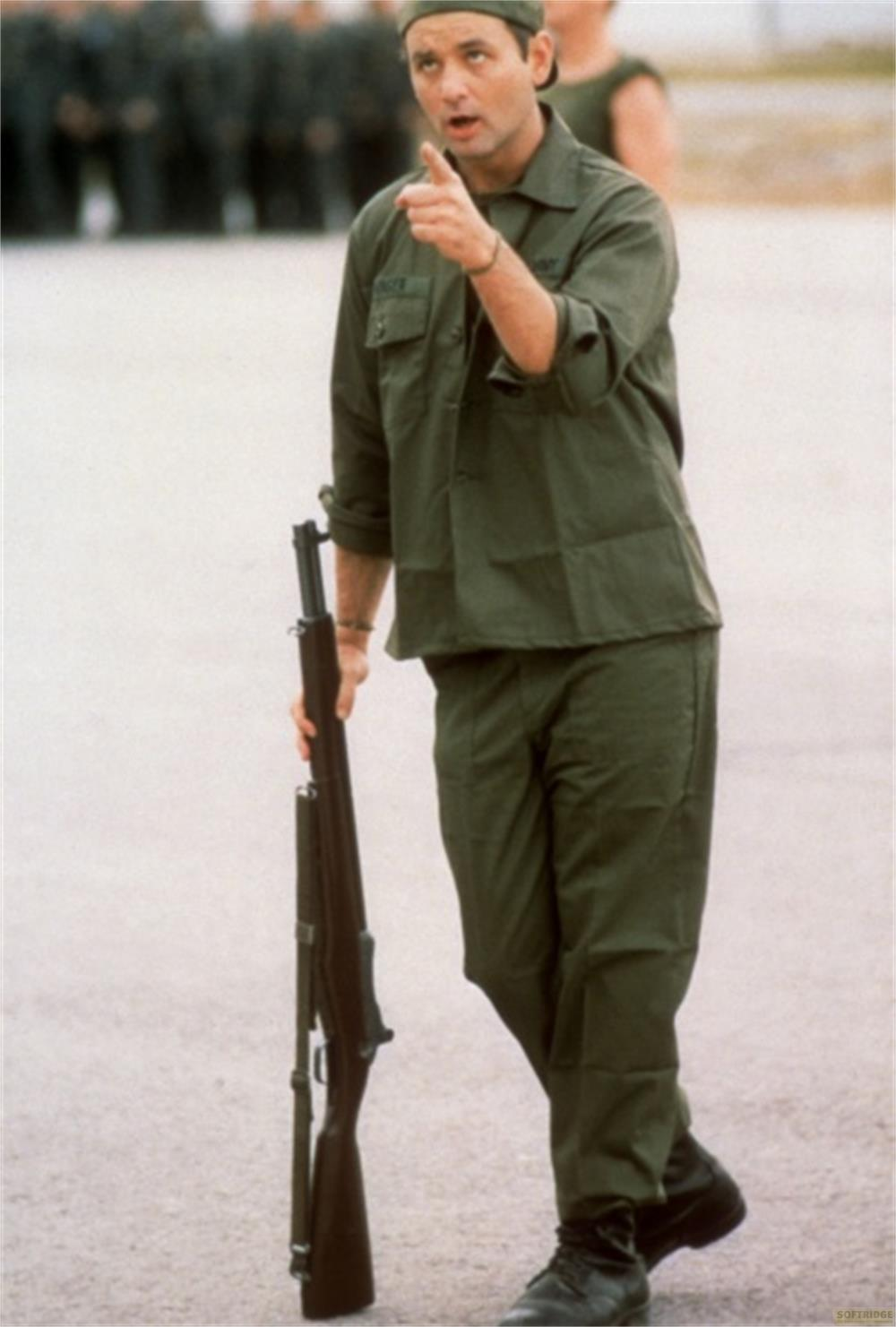 Un homme en uniforme pointe du doigt en tenant un fusil. Soldats en arrière-plan.