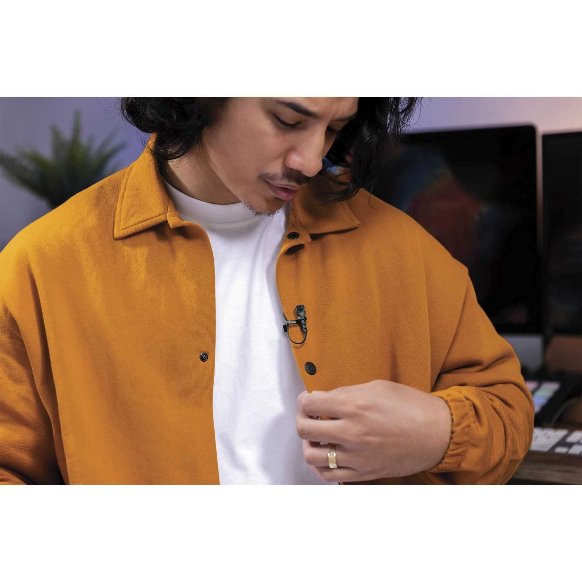 Mężczyzna z wąsami i otwartą pomarańczową koszulą nosi mikrofon krawatowy.