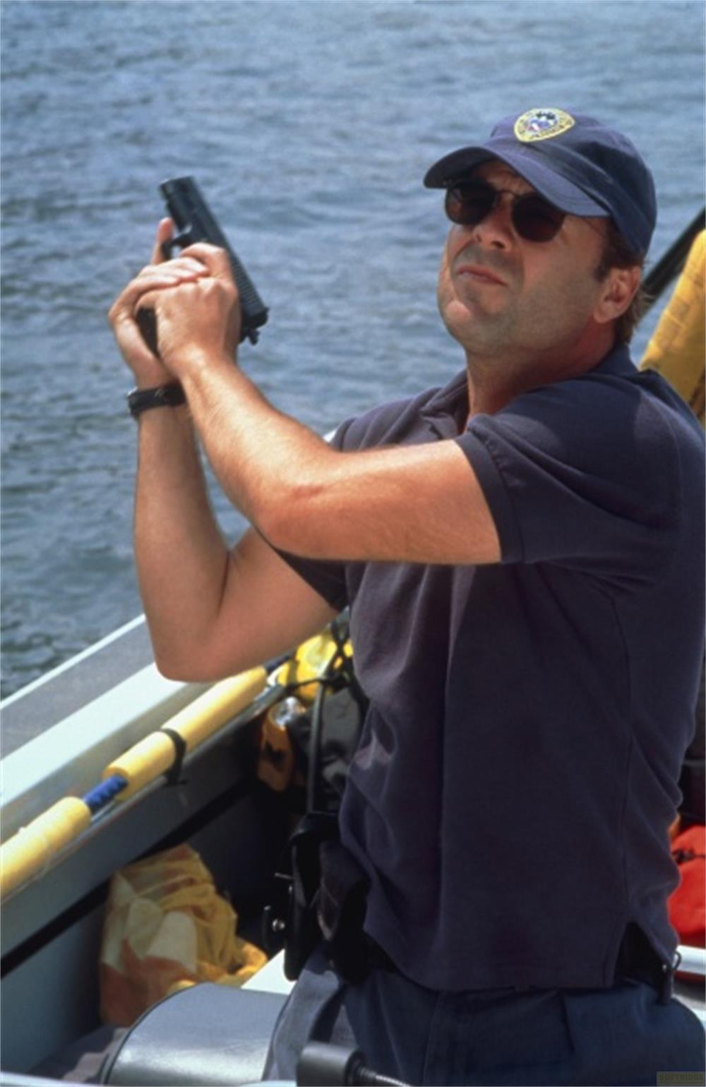 Un homme en polo bleu et casquette tient un pistolet sur un bateau.